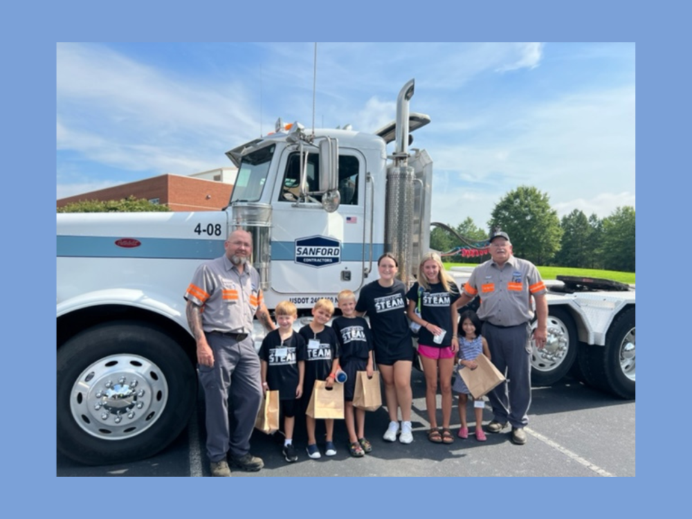 Two SCI Employees with group of children in front of truck