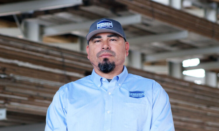 Photo of Luis Sanchez in a warehouse space wearing a Sanford Contractor hat and shirt.