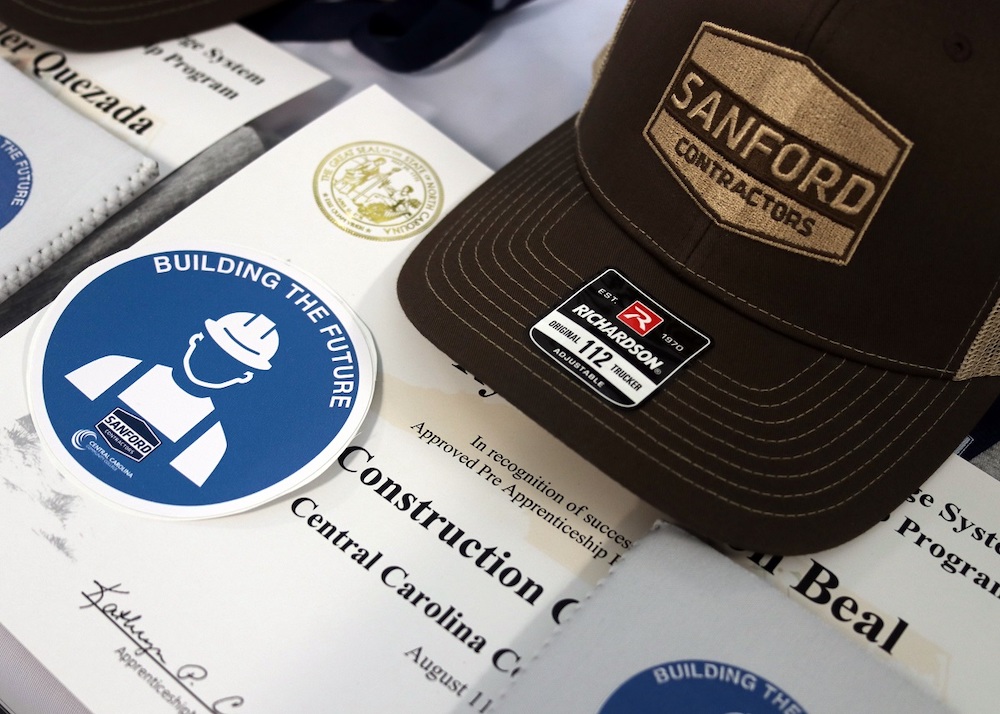 Close up shot of Sanford Contractors hat alongside the certificate from the SCI Construction Academy.