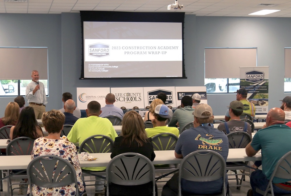 Zac West speaking into microphone in front of all the participates of the SCI Construction Academy.